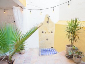 Une cour avec un sol carrelé, des plantes en pot, une porte décorative et des guirlandes lumineuses.