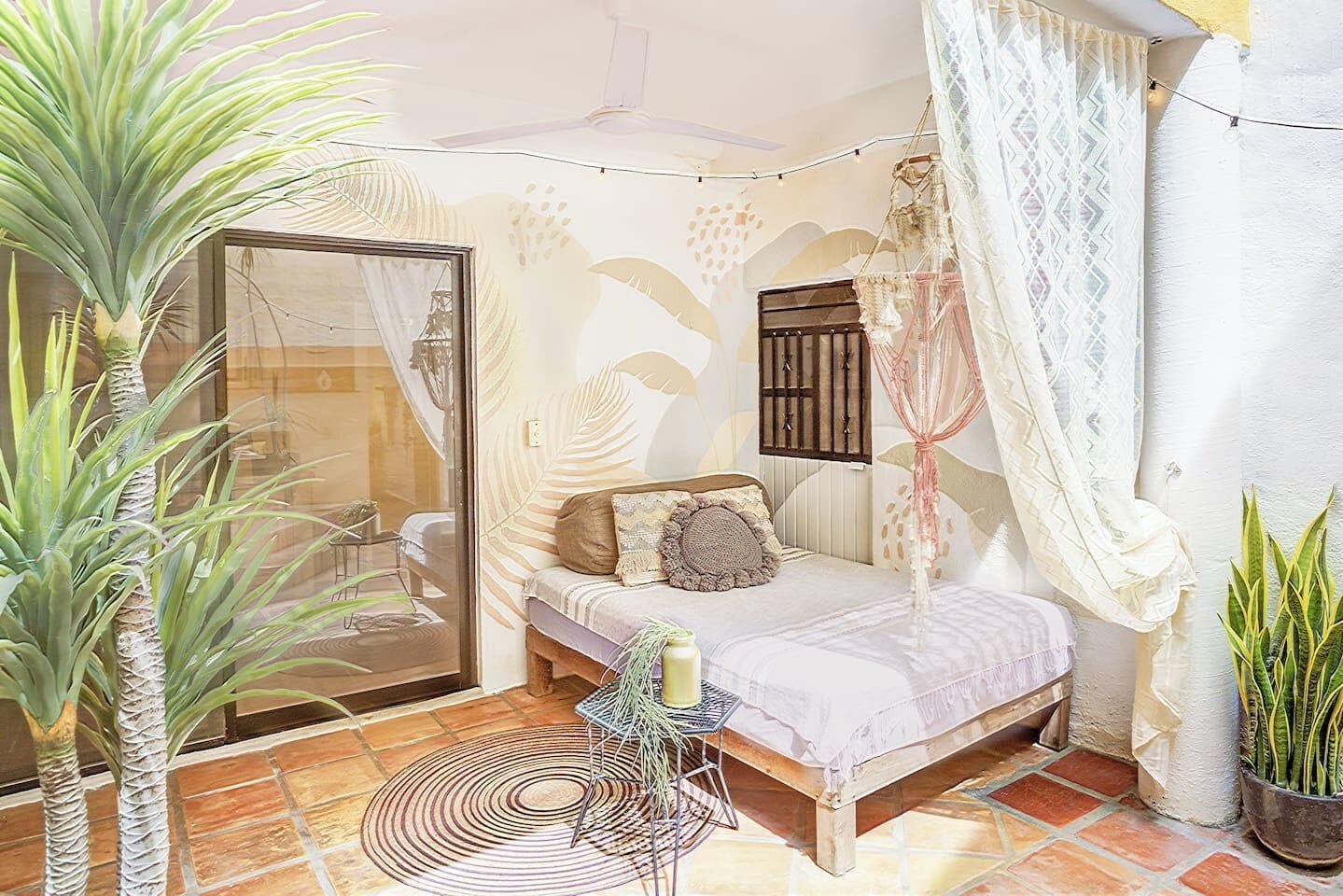 A bedroom with a bed, a small table, a potted plant, and a window with curtains.