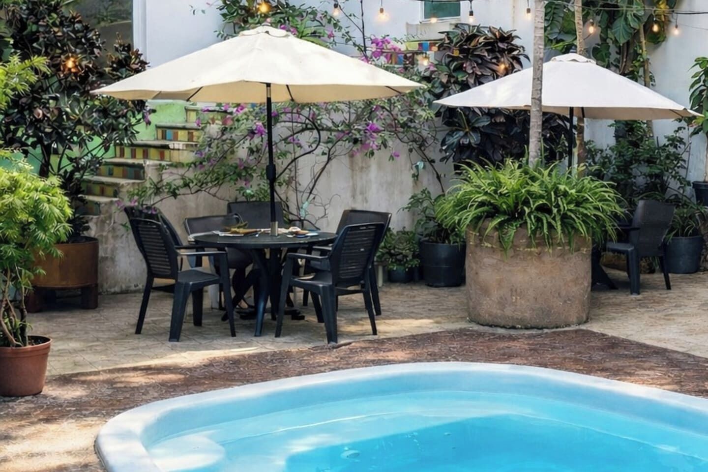 A poolside area with a round table and chairs, two umbrellas, and potted plants.