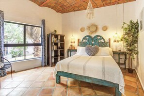 Un dormitorio con cama, una estantería, una ventana y una planta.