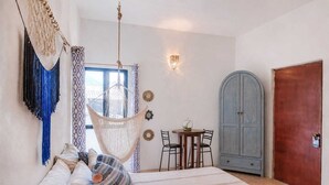 A room with a bed, a hanging chair, a table with chairs, a cabinet, and a door. - Pool Access • Walk to Beach • Kitchen • 
SAYULITA BOUTIQUE SUITES - 2 (Sayulita)