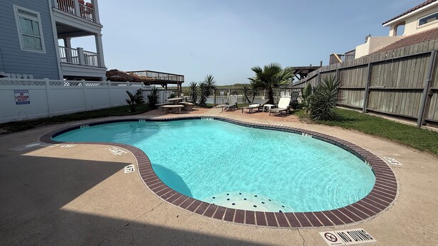 A swimming pool with a wooden deck, lounge chairs, and a wooden fence. - Cozy Condo with Pool - Walk2Beach - Boat Slip - Sleeps 4 (Corpus Christi)