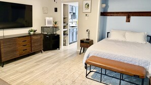A modern bedroom with a large bed, a bench, a TV, a ceiling fan, and a kitchenette. - Cozy Condo with Pool - Walk2Beach - Boat Slip - Sleeps 4 (Corpus Christi)
