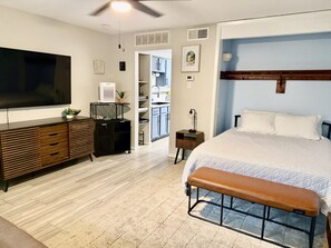 A modern bedroom with a large bed, a bench, a TV, a ceiling fan, and a kitchenette. - Cozy Condo with Pool - Walk2Beach - Boat Slip - Sleeps 4 (Corpus Christi)