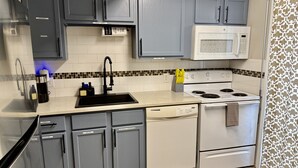 A kitchen with grey cabinets, a white stove, and a microwave. - Cozy Condo with Pool - Walk2Beach - Boat Slip - Sleeps 4 (Corpus Christi)