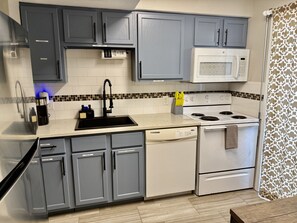 A kitchen with grey cabinets, a white stove, and a microwave. - Cozy Condo with Pool - Walk2Beach - Boat Slip - Sleeps 4 (Corpus Christi)