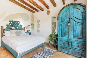 A bedroom with a bed, a wardrobe, a bedside table, a hanging plant, and a wall with decorative plates. - Pool Access • Walk to Beach • Kitchen • 
SAYULITA BOUTIQUE SUITES - 3 (Sayulita)