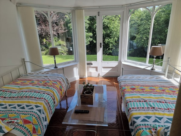 Une chambre avec deux lits, une table en verre et une vue sur un jardin grâce à de grandes fenêtres.