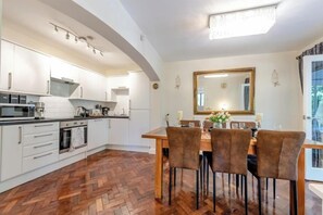 Una cocina con armarios blancos, una mesa de comedor de madera con sillas y un espejo grande sobre la mesa.