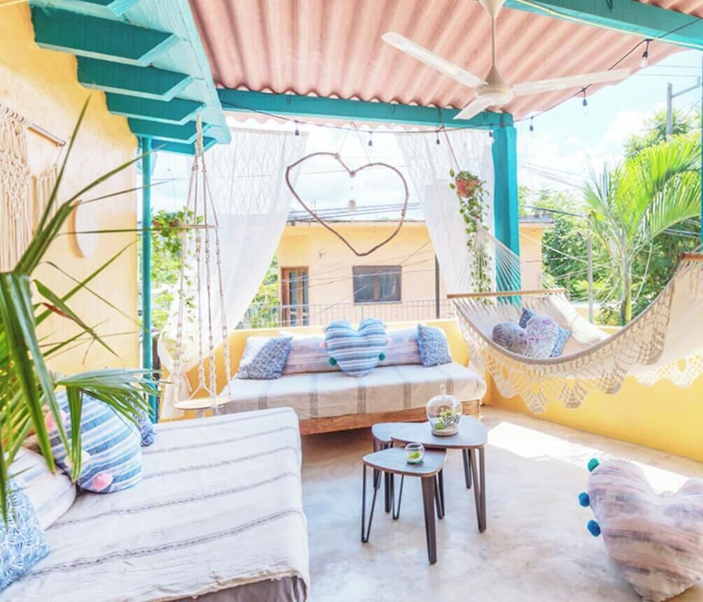 A covered outdoor seating area with a hammock, a cushioned bench, and a small table.