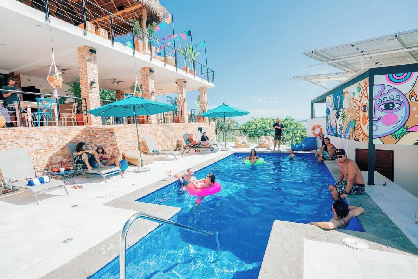 En swimmingpool med liggestole, parasoller og et muralmaleri på væggen.
