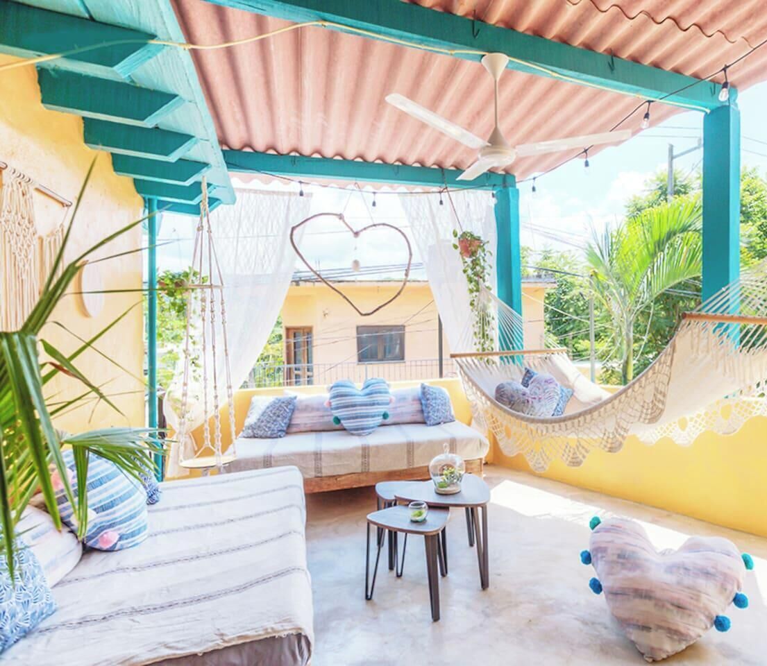 A covered outdoor seating area with a hammock, a cushioned bench, and a small table.
