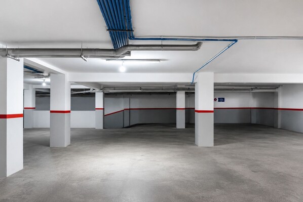 Useita kerroksia sisältävä pysäköintihalli, jossa on betonilattiat, valkoiset pilarit ja punaiset turvamerkinnät.