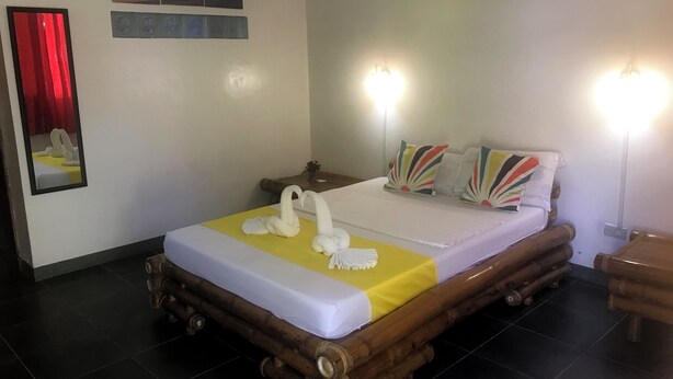 A bed with a yellow bedspread, white pillows, and a swan decoration. There are wall-mounted lights and a mirror on the wall.