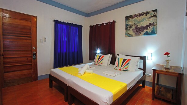 A hotel room with a wooden bed, a yellow bedspread, a ceiling fan, a painting on the wall, and a wooden door. - Beautiful, spacious, resort with a secluded garden. (Santander)