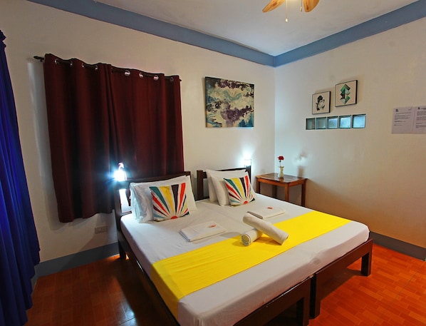 Una habitación de hotel con cama, cortinas, un cuadro, una mesita con un florero y una pared con fotografías enmarcadas.