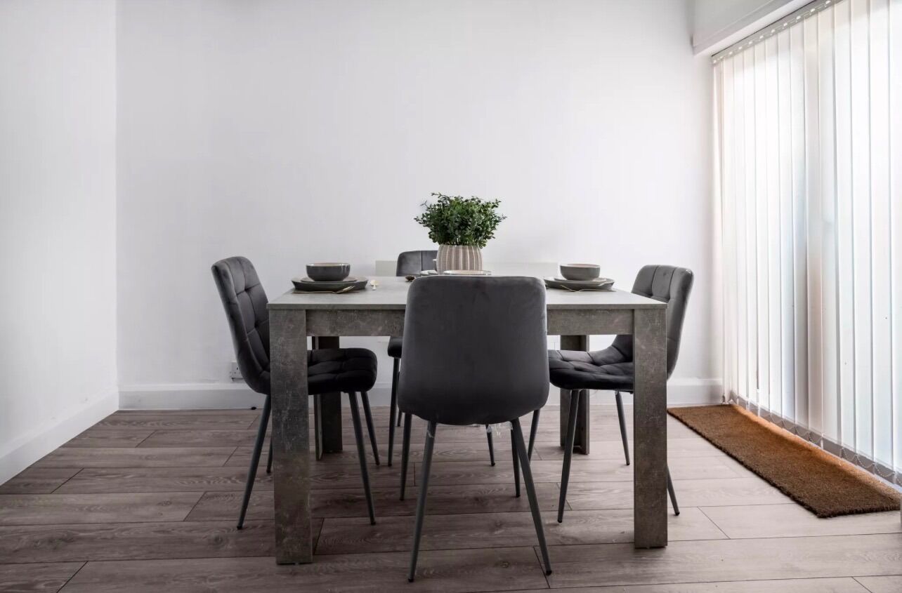 Un comedor con una mesa, sillas, una planta en maceta y un ventanal con persianas.