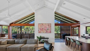 A spacious living area with a large sectional sofa, a dining table with chairs, and a kitchen area with a bar. - 6 Karboora Drive - Luxury holiday home with pool (Point Lookout)