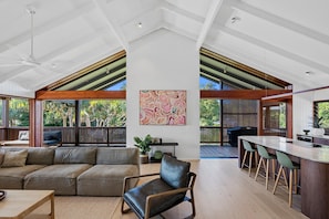 A spacious living area with a large sectional sofa, a dining table with chairs, and a kitchen area with a bar. - 6 Karboora Drive - Luxury holiday home with pool (Point Lookout)