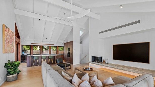 A modern living room with a large grey sofa, a flat-screen TV, and a kitchen area in the background. - 6 Karboora Drive - Luxury holiday home with pool (Point Lookout)