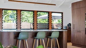 A modern kitchen with a bar area, wooden cabinets, and large windows. - 6 Karboora Drive - Luxury holiday home with pool (Point Lookout)