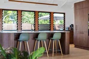 A modern kitchen with a bar area, wooden cabinets, and large windows. - 6 Karboora Drive - Luxury holiday home with pool (Point Lookout)