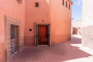 A narrow alleyway with a wooden door and a metal gate, leading to a building with a pink facade. - Riad Romouz Bab Ahmar (Marrakech)
