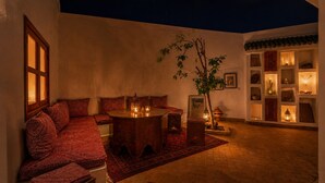 Et hyggeligt rum med en sofa, et rundt bord med stearinlys, en potteplante og reoler med dekorative genstande.