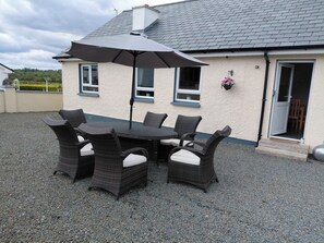 A patio with a table and chairs, a large umbrella, and a house with a grey roof and white walls.