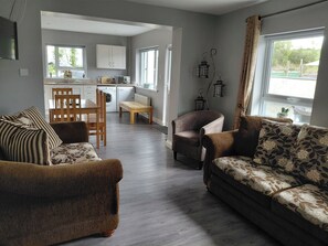 A living room with a sofa, a chair, a dining table, and a kitchen in the background.