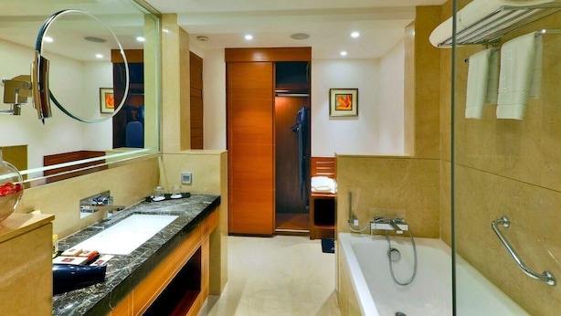 A modern bathroom with a large mirror, a bathtub, a shower, and a vanity with a sink. - Madin (Varanasi)