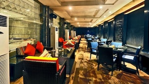 A restaurant with a long counter, seating area with sofas and chairs, and a patterned wall. - Madin (Varanasi)