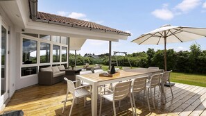 Eine überdachte Terrasse im Freien mit Holztisch und -stühlen, einer Schaukel und Blick auf die umliegende Grünfläche.