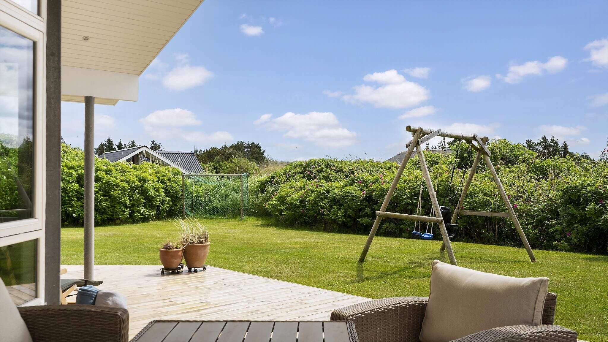 Eine Terrasse mit Gartenmöbeln, einer Schaukel und Kübelpflanzen.