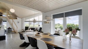 Ruime eethoek met een lange tafel, moderne stoelen en grote ramen met uitzicht op groen.