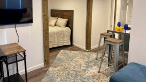 A bedroom with a bed, a TV, a desk with a chair, and a bathroom visible through an open door. - Cozy lower-level 1 bedroom studio in NOLA with Private Covered Outdoor Patio (New Orleans)