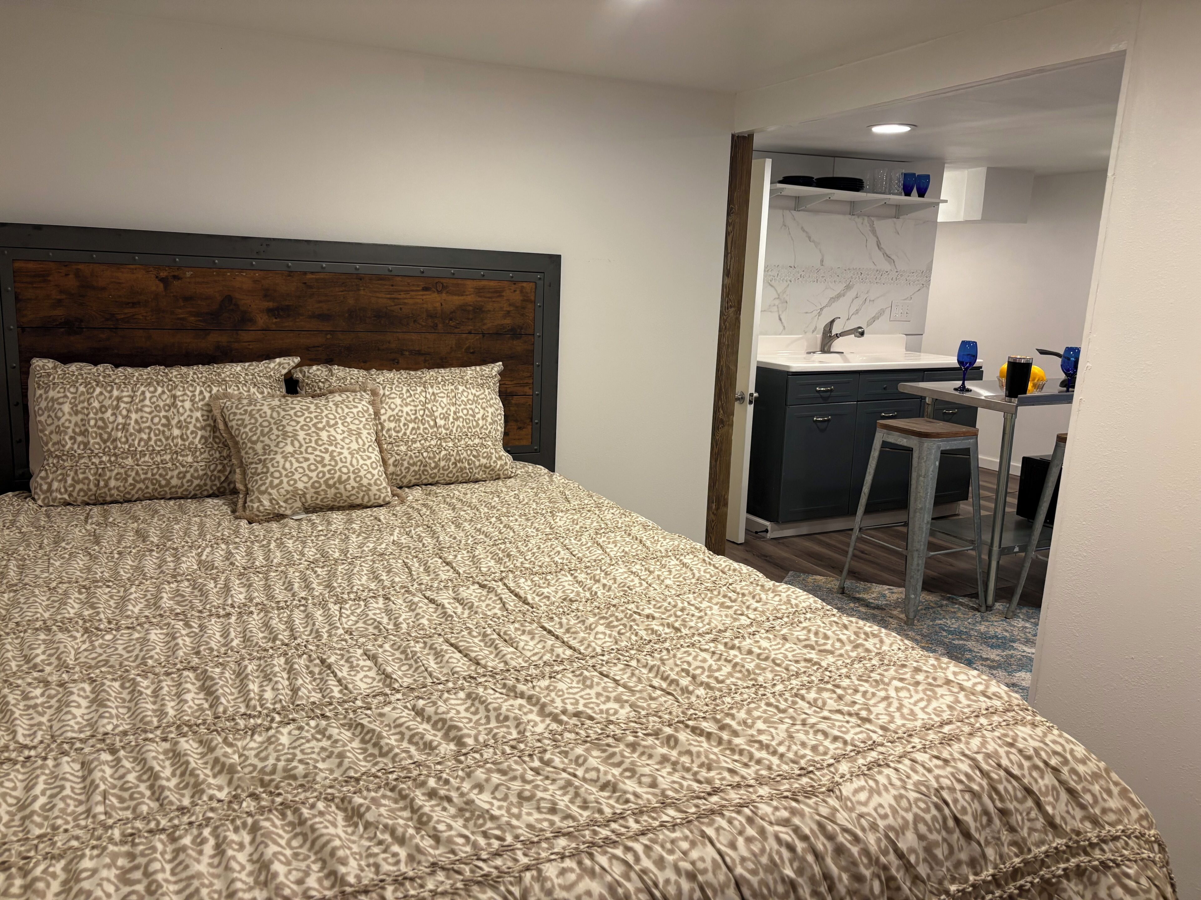 Een slaapkamer met een bed, een hoofdeinde en een klein kitchenette voorzien van een spoelbak en kastjes.