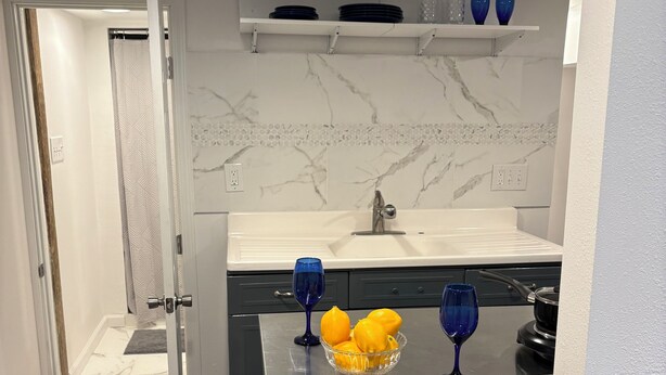 A compact kitchen with a marble backsplash, a sink, a stove, and two stools. - Cozy lower-level 1 bedroom studio in NOLA with Private Covered Outdoor Patio (New Orleans)