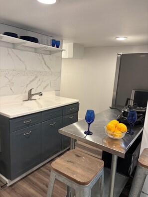A modern kitchen with a marble backsplash, stainless steel appliances, and a wooden stool. - Cozy lower-level 1 bedroom studio in NOLA with Private Covered Outdoor Patio (New Orleans)