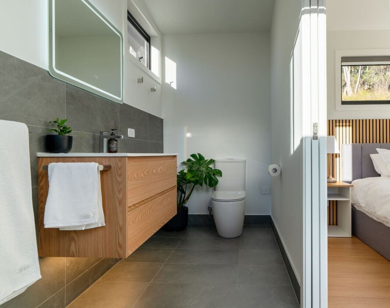 A modern bathroom with a wooden vanity, a toilet, and a shower area.