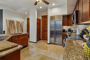 Una cucina con piani di lavoro in granito, mobili in legno, frigorifero in acciaio inossidabile e una ventola a soffitto.