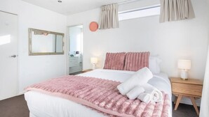 Quarto com cama, mesas de cabeceira, espelho e janela com cortinas.