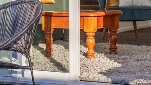 Quarto com porta de vidro que dá para uma escadaria, mesa de madeira com cadeiras e sofá com almofadas.