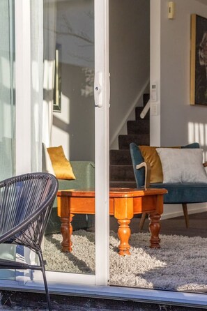 Ein Zimmer mit Glastür zu einer Treppe, einem Holztisch mit Stühlen und einem Sofa mit Kissen.