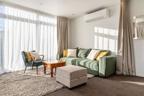 Ein Wohnzimmer mit einem grünen Sofa, einem Sessel, einem kleinen Tisch und einem Hocker.
