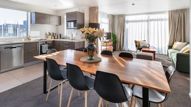 Uma sala de estar moderna com área de refeições, cozinha e janelas amplas.