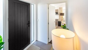 Corredor com porta escura, uma luminária e vislumbre de uma cozinha.