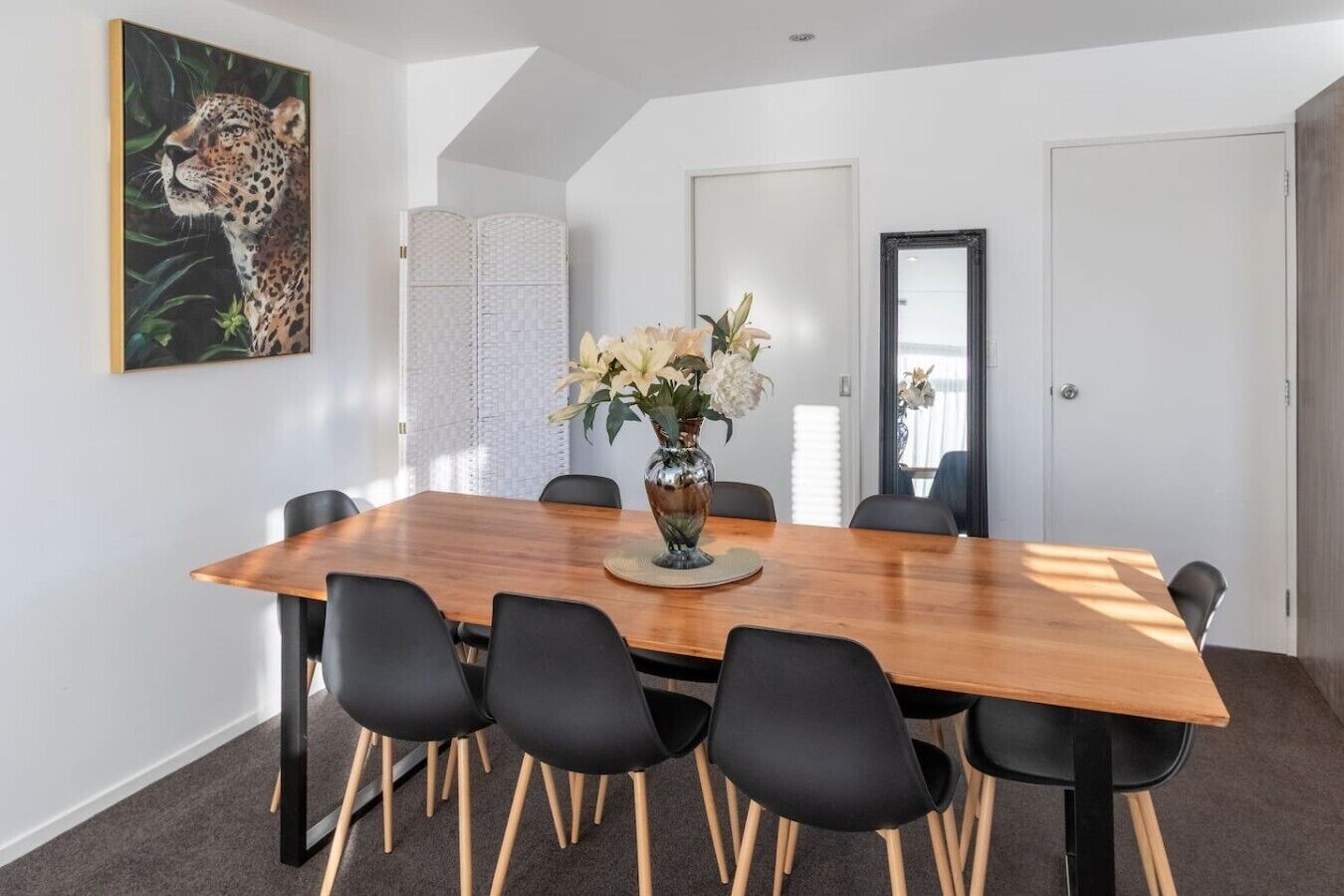 A conference room with a wooden table, black chairs, a vase with flowers, and a leopard painting on the wall.