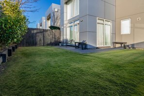 Ein modernes Gebäude mit gepflegter Rasenfläche, Holzzaun und Sitzgelegenheiten im Freien.