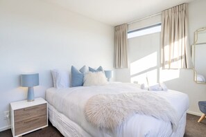 Ein Schlafzimmer mit einem Bett, Nachttischen, einer Lampe, einem Spiegel und einem Fenster mit Vorhängen.